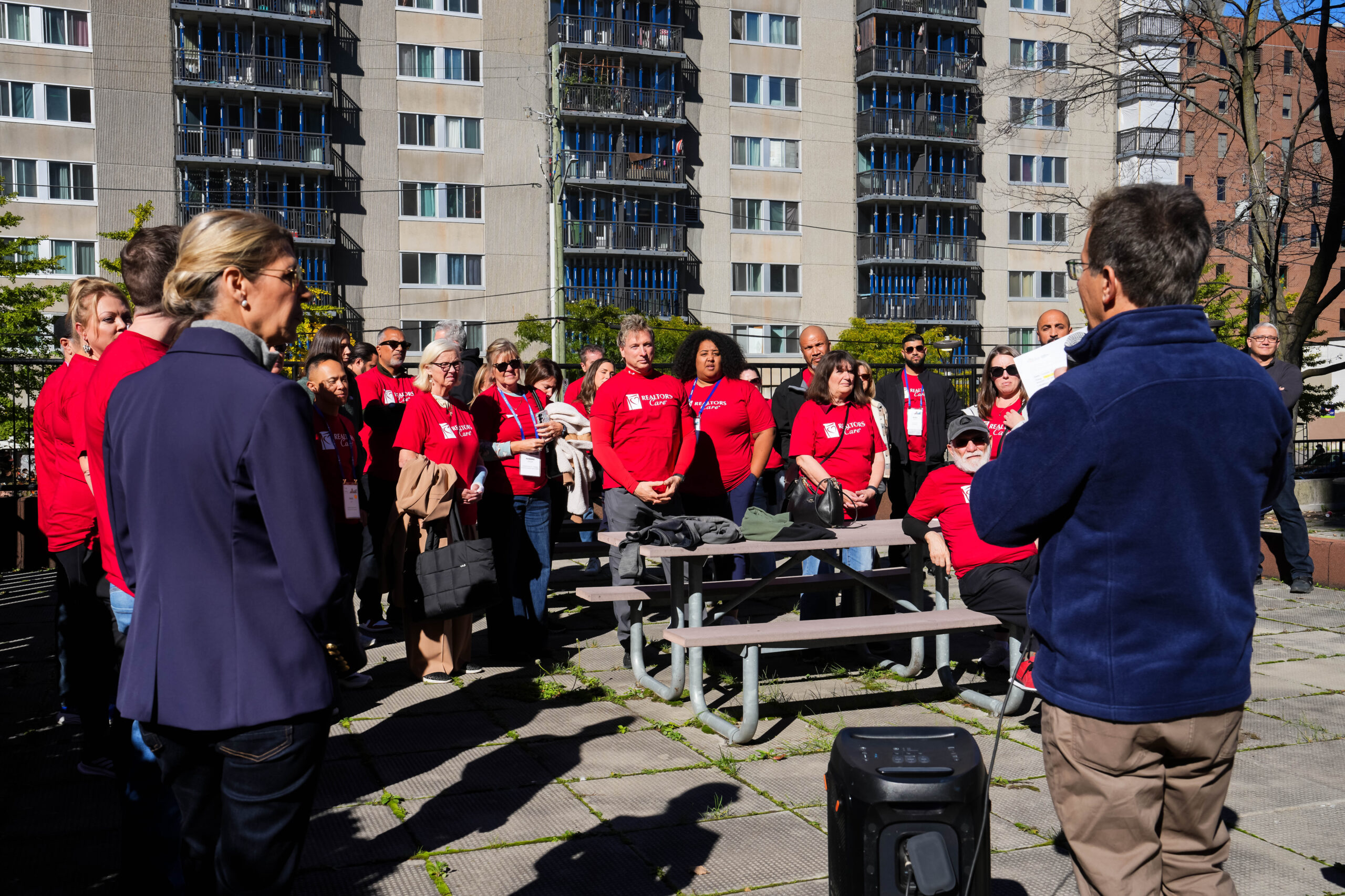 Volunteers in red REALTORS Care shirts listening to an outdoor briefing.